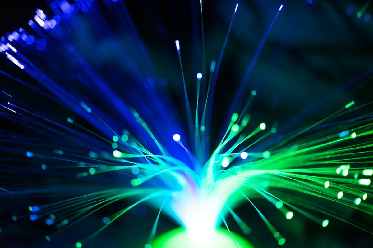 Fibras ópticas iluminadas con luz que representa la transmisión de datos como pulsos de fotones a través del núcleo de cristal de sílice de la fibra monomodo, con atenuación mínima de 0.20 dB/km